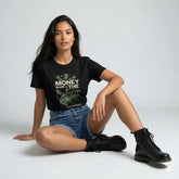 Woman wearing a black t-shirt with text and denim shorts, sitting on the floor against a plain background
