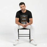 Man sitting on a chair wearing a black t-shirt with text, white pants, and white sneakers on a white background