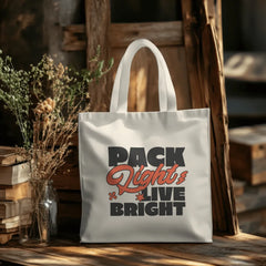 Tote bag with 'Pack Light Live Bright' text on a wooden surface with books and plants.
