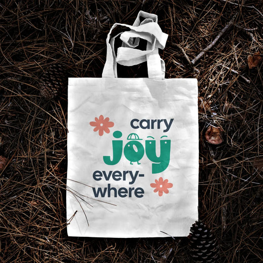 Tote bag with 'carry joy everywhere' text on a natural background