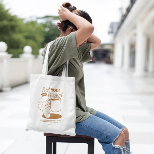 Person sitting outdoors with a tote bag featuring 'Fuel Your Passion' text and graphic.