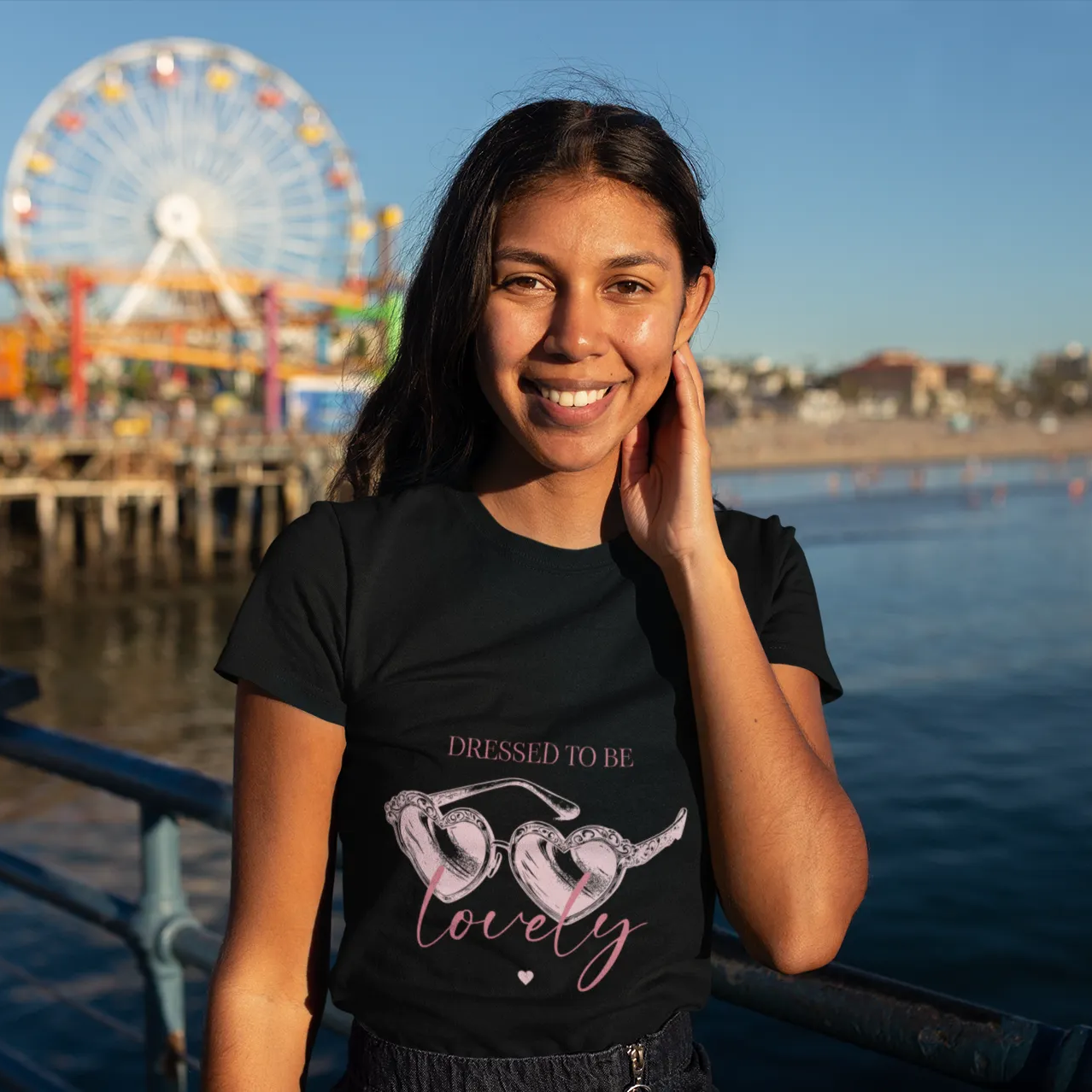 Woman wearing a black t-shirt with a quote, standing by water with a Ferris wheel in the background