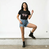 Woman wearing a black t-shirt with a graphic design, denim shorts, and black boots on a white background