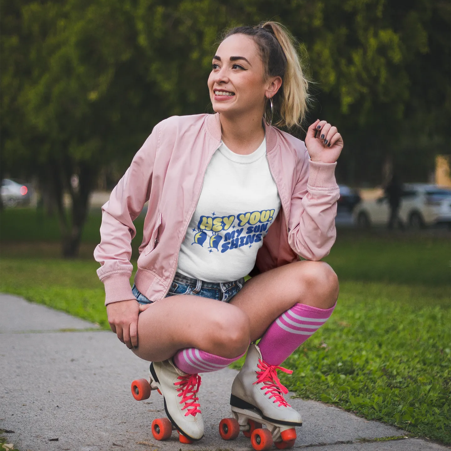 Woman in pink jacket and roller skates posing on a sidewalk with greenery in the background
