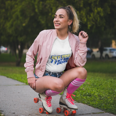 Woman in pink jacket and roller skates posing on a sidewalk with greenery in the background
