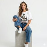 Woman wearing a t-shirt with a graphic design and text, sitting on a bed with a cat.