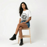 Woman sitting on a chair wearing a white t-shirt with text and denim shorts.