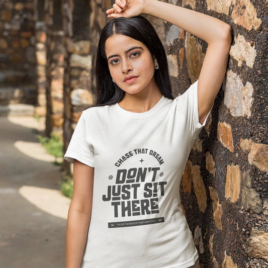Woman wearing a white t-shirt with text, leaning against a stone wall.