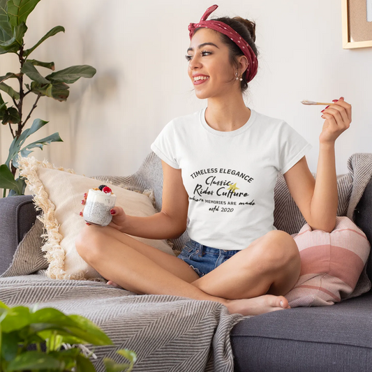 Woman sitting on a couch holding a mug and a cigarette, wearing a white t-shirt with text.