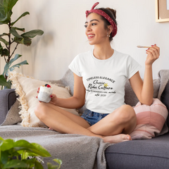 Woman sitting on a couch holding a mug and a cigarette, wearing a white t-shirt with text.