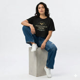 Person wearing a black t-shirt with text and graphics, sitting on a concrete block against a white background