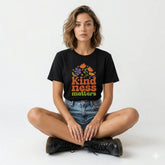 Woman wearing a black t-shirt with 'Kindness Matters' text and flowers, sitting on a bicycle.