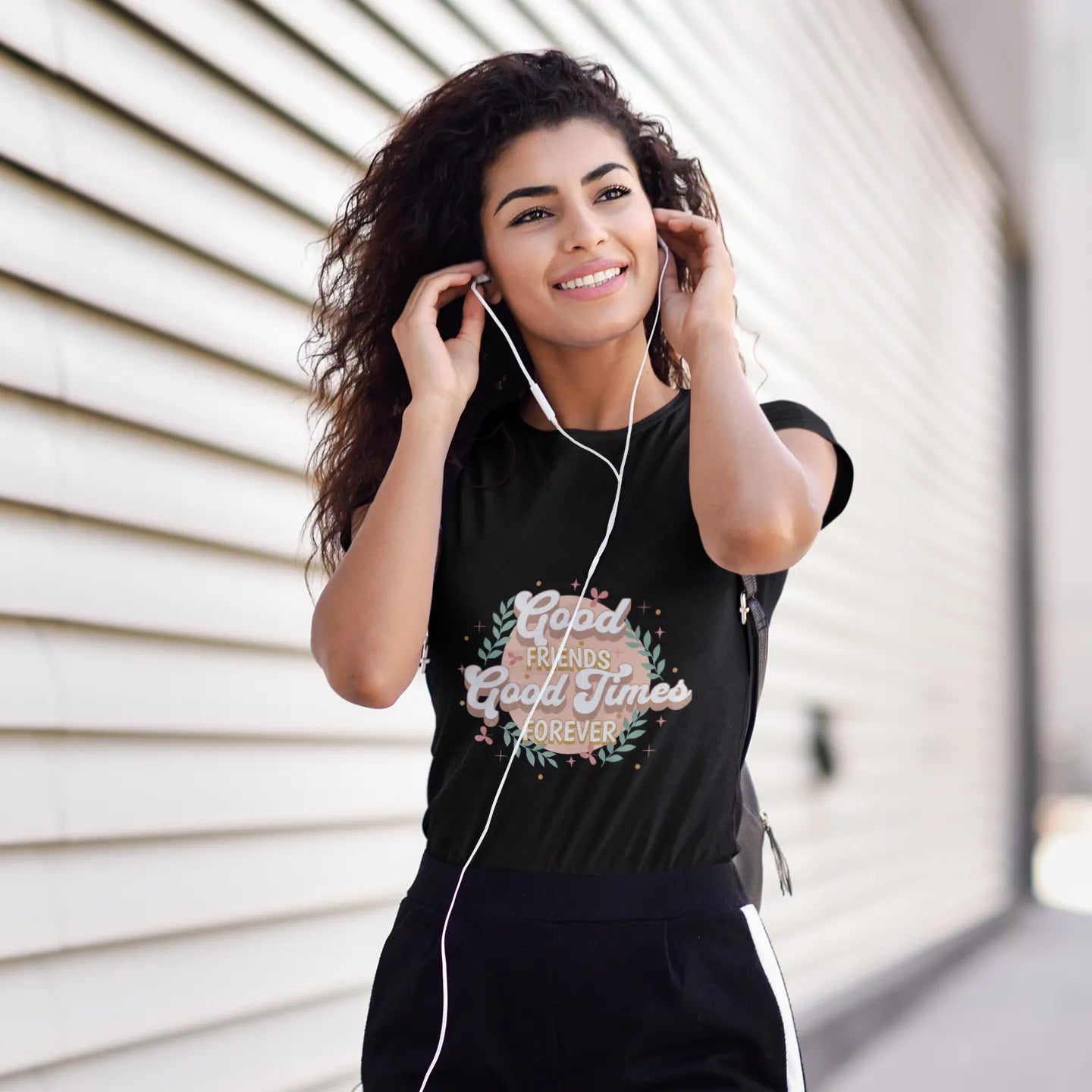 Woman wearing a black t-shirt with text and headphones, standing against a light-colored wall.
