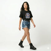 Woman wearing a black t-shirt with a graphic design, blue denim shorts, and black boots on a white background