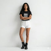 Person wearing a black t-shirt with text, white shorts, and black boots on a light gray background