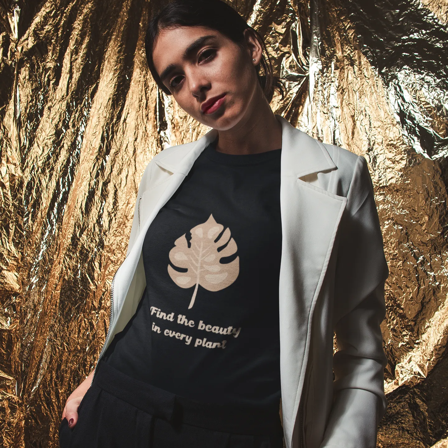 Woman wearing a black t-shirt with a leaf design and text, standing against a gold leafy background.