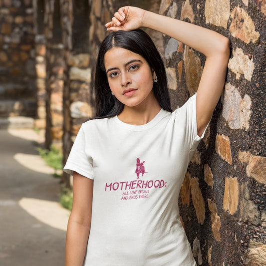 Woman wearing a white t-shirt with a graphic and text, standing against a stone wall.