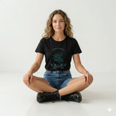 Woman wearing a black t-shirt with green text and denim shorts sitting on a white background