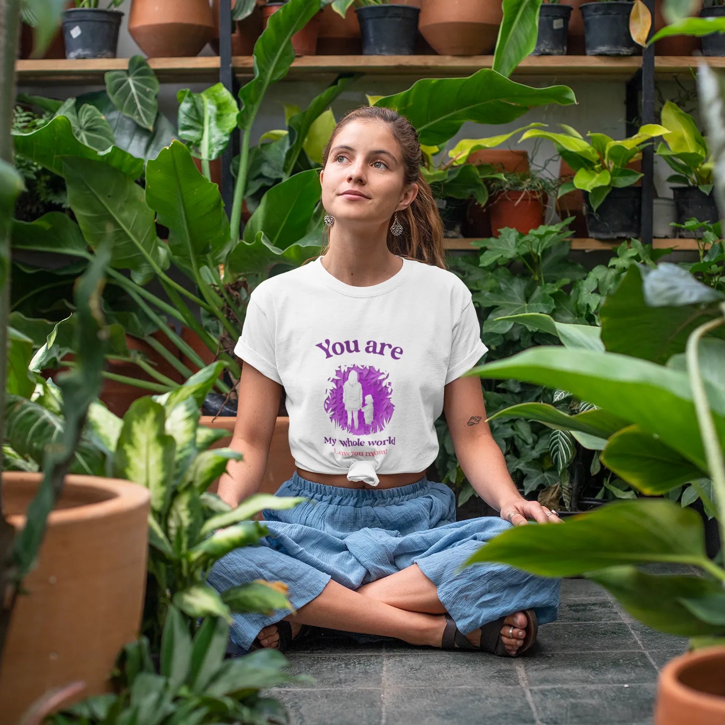 Woman sitting among plants wearing a t-shirt with a motivational quote.