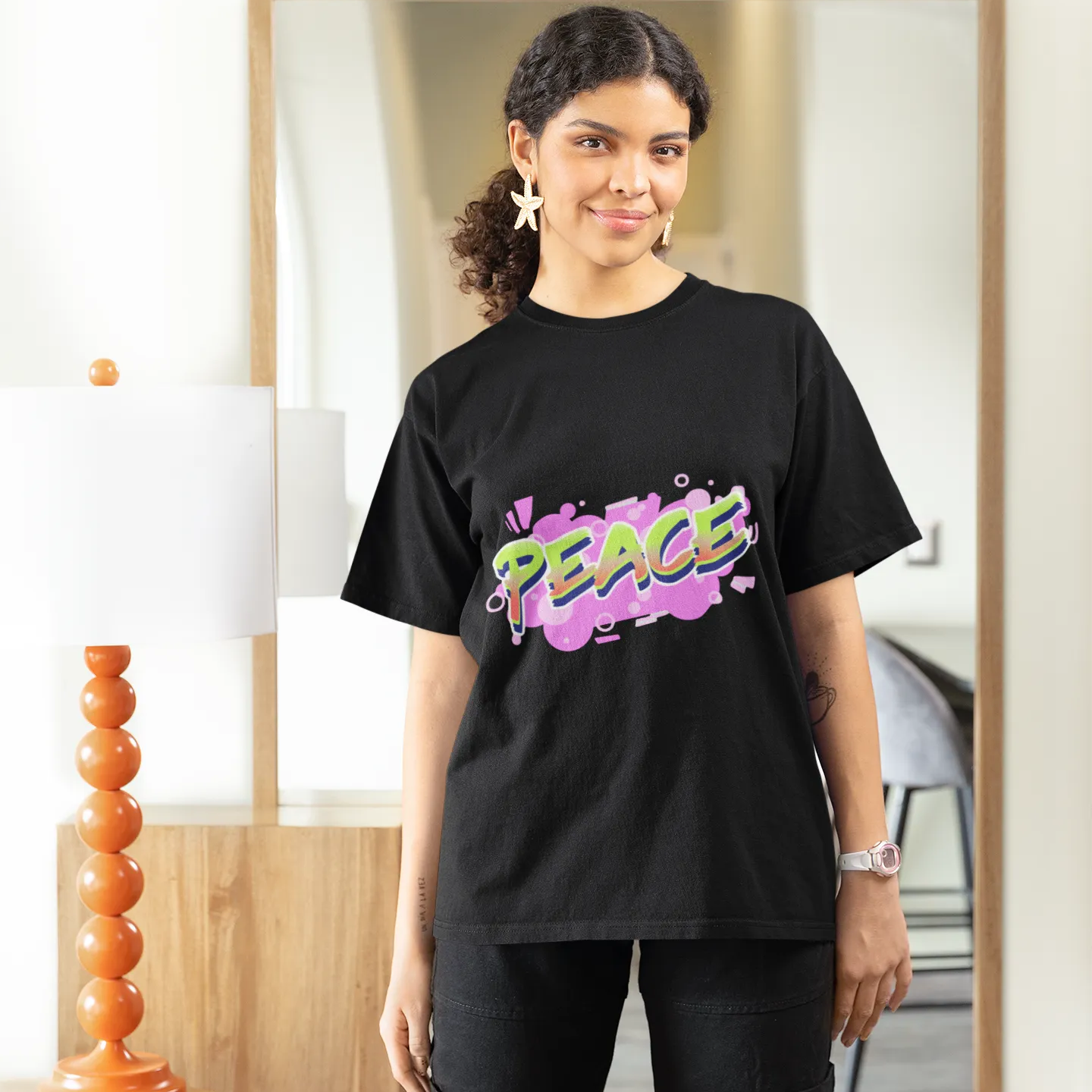 Person wearing a black t-shirt with colorful text, standing in a room.