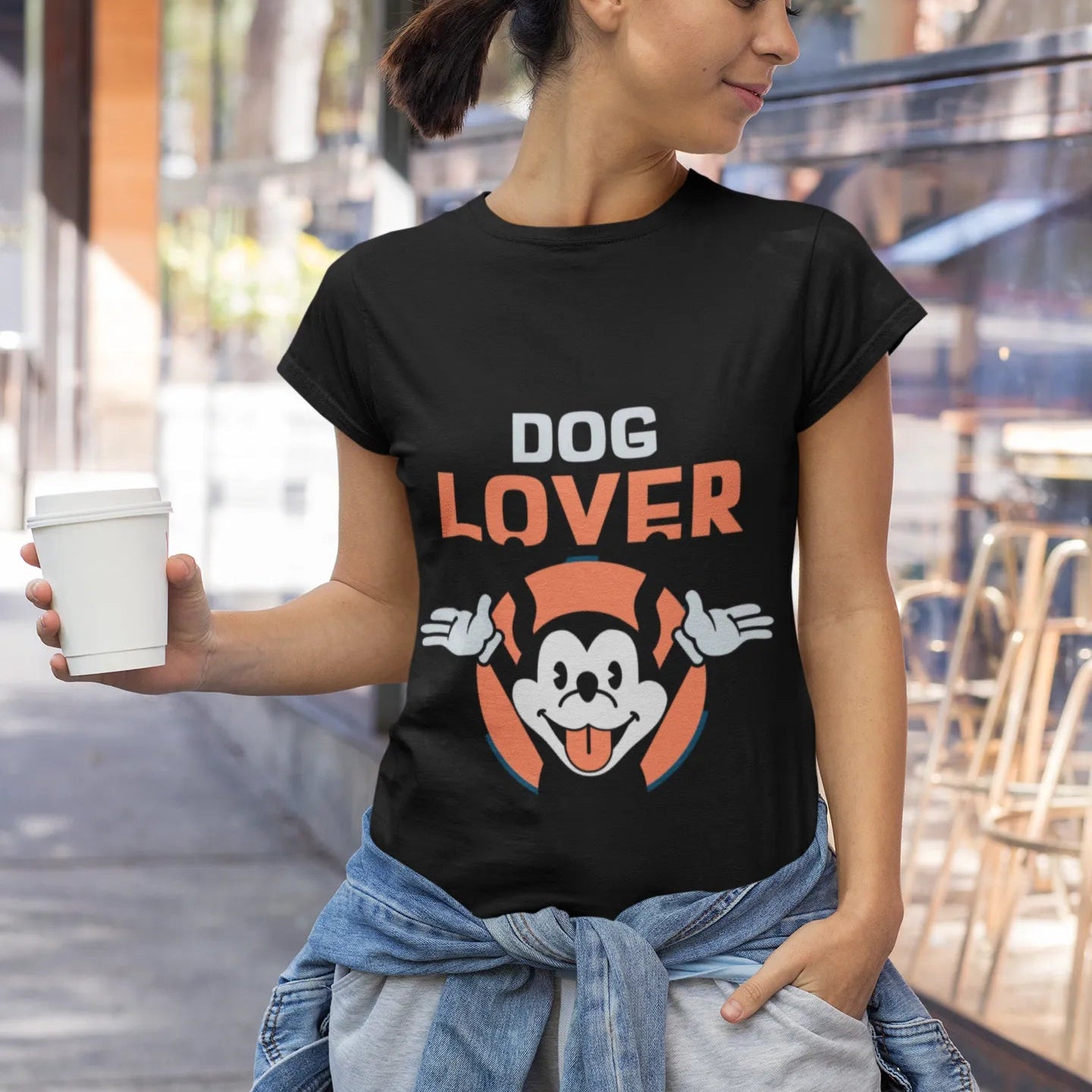 Woman wearing a black t-shirt with 'DOG LOVER' and a cartoon dog graphic, holding a cup outdoors.