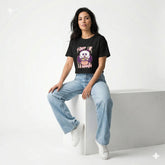 Woman wearing a black t-shirt with a graphic design and blue jeans sitting on a white block.