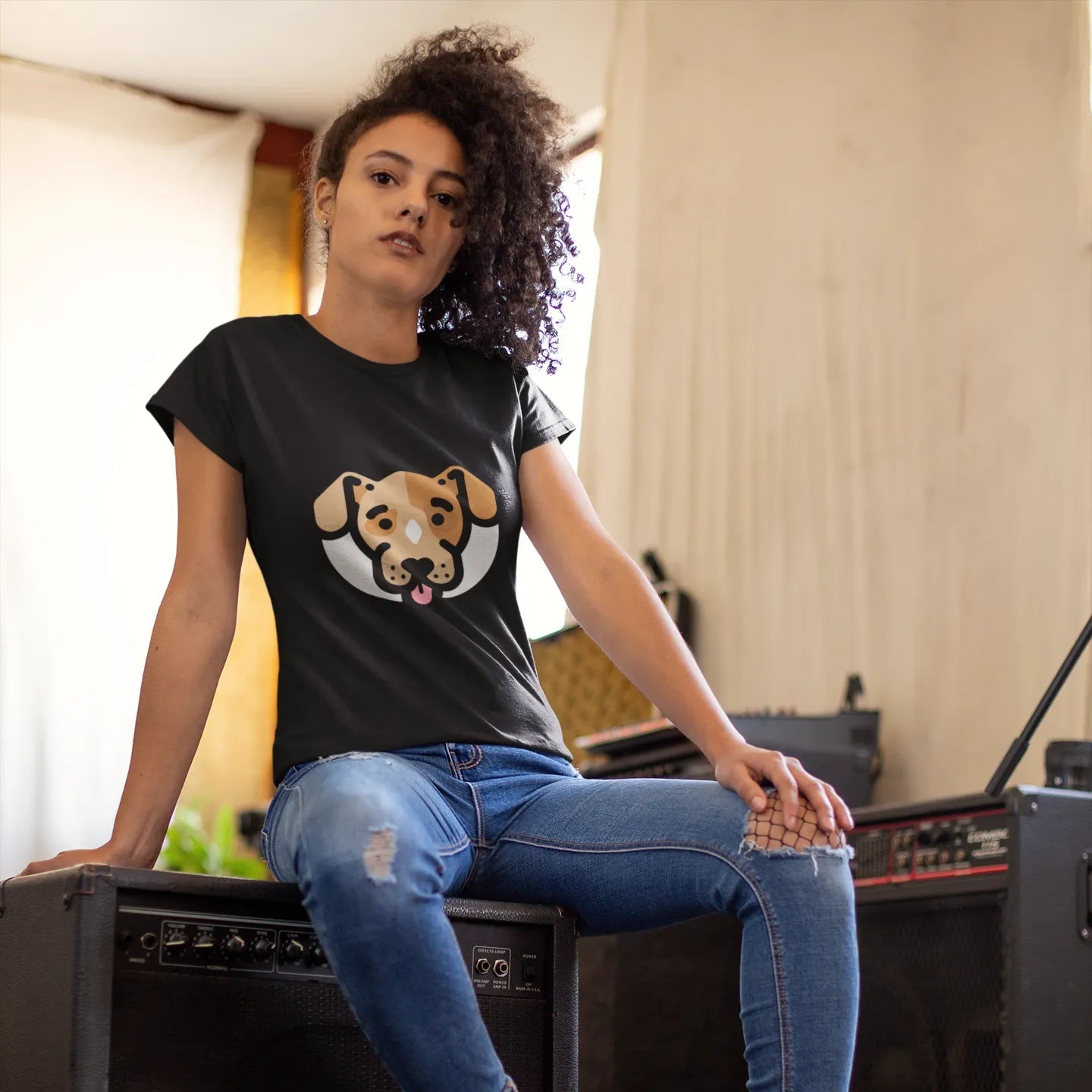 Woman sitting on a speaker wearing a black t-shirt with a dog graphic and blue jeans.