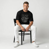 Man sitting on a chair wearing a black t-shirt with text and white pants on a light gray background