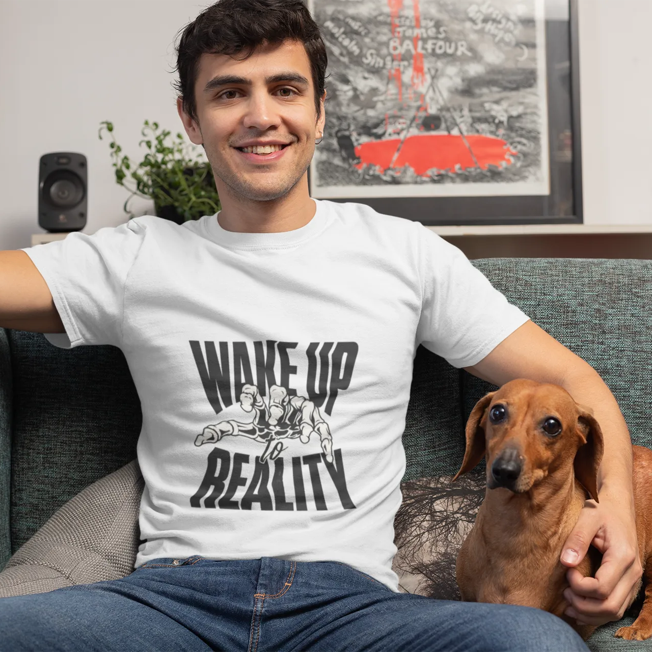Man wearing a t-shirt with 'Wake Up Reality' graphic sitting on a couch with a dog.