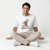Man sitting cross-legged wearing a white t-shirt with a graphic and text.