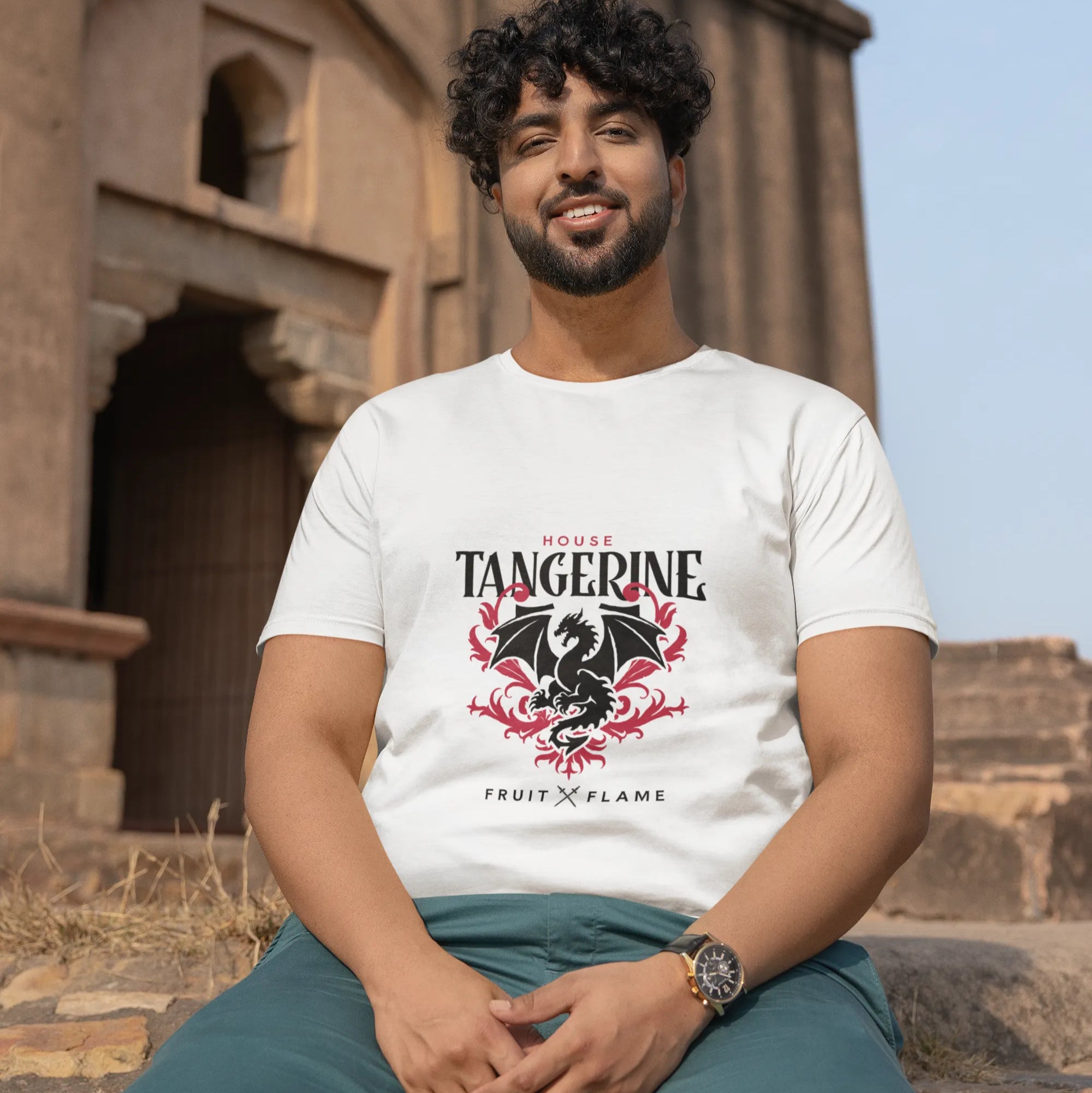 Man wearing a white t-shirt with a dragon design sitting in front of an ancient architectural structure.