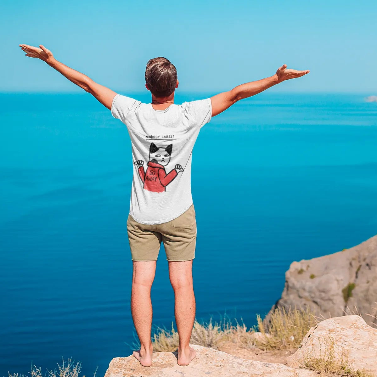 Person standing on a cliff overlooking a blue sea with arms outstretched