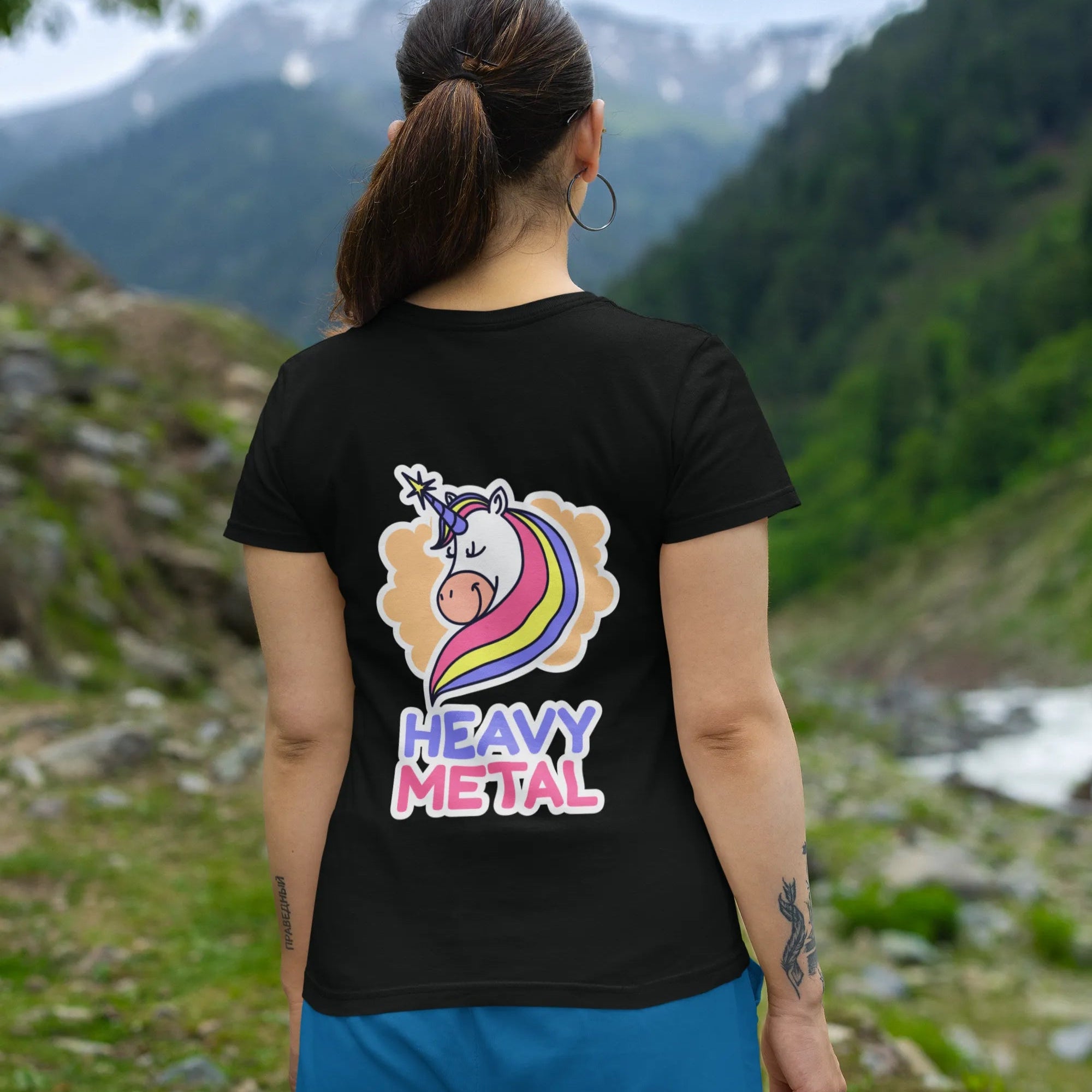 Person wearing a black t-shirt with a colorful unicorn design and 'Heavy Metal' text, standing in a mountainous landscape.