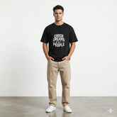 Man wearing a black t-shirt with 'Chase dreams not people' text, standing indoors with plants in the background.