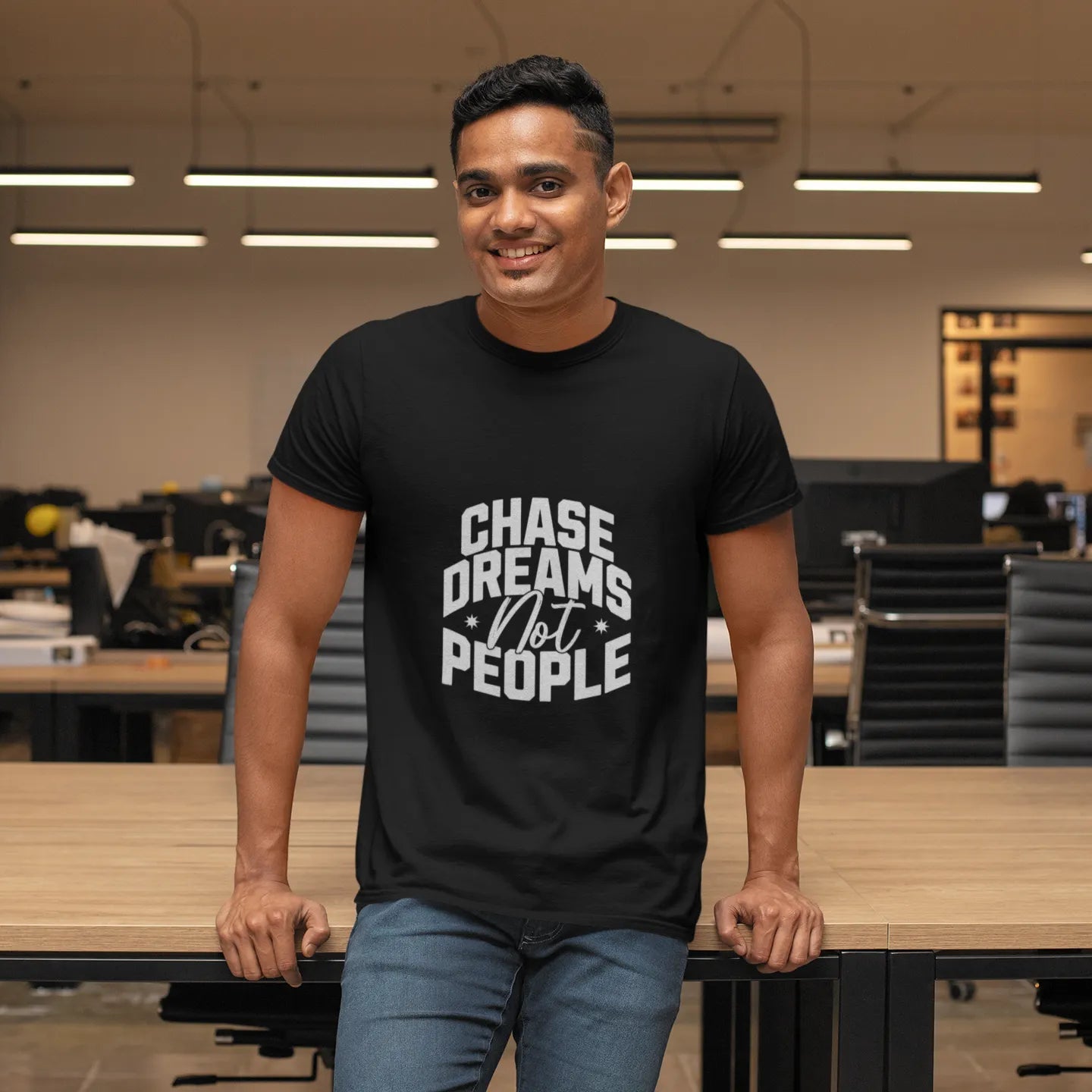 Man wearing a black t-shirt with 'Chase Dreams Not People' text in an office setting