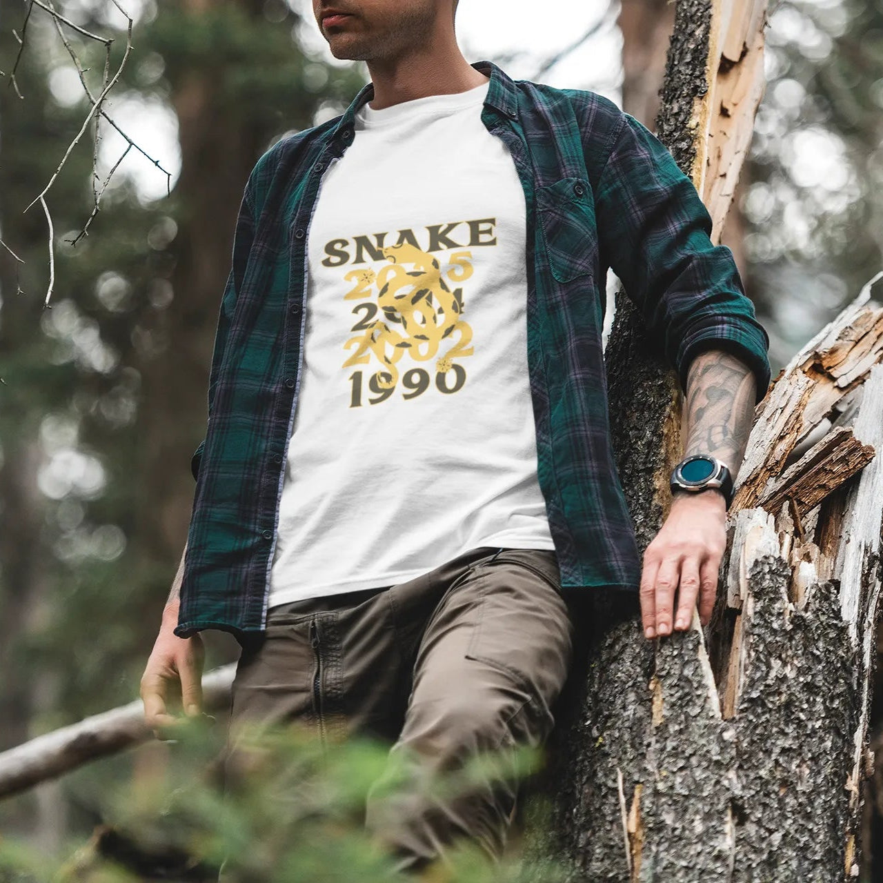 Person wearing a white t-shirt with 'Snake 1990' design in a forest setting