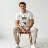 Man wearing a white t-shirt with a coffee graphic and text against a blue tiled wall.