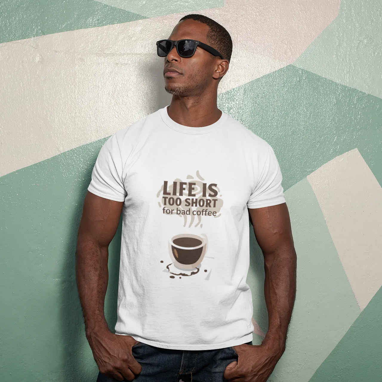Man wearing a white t-shirt with a coffee graphic and text against a geometric-patterned wall.