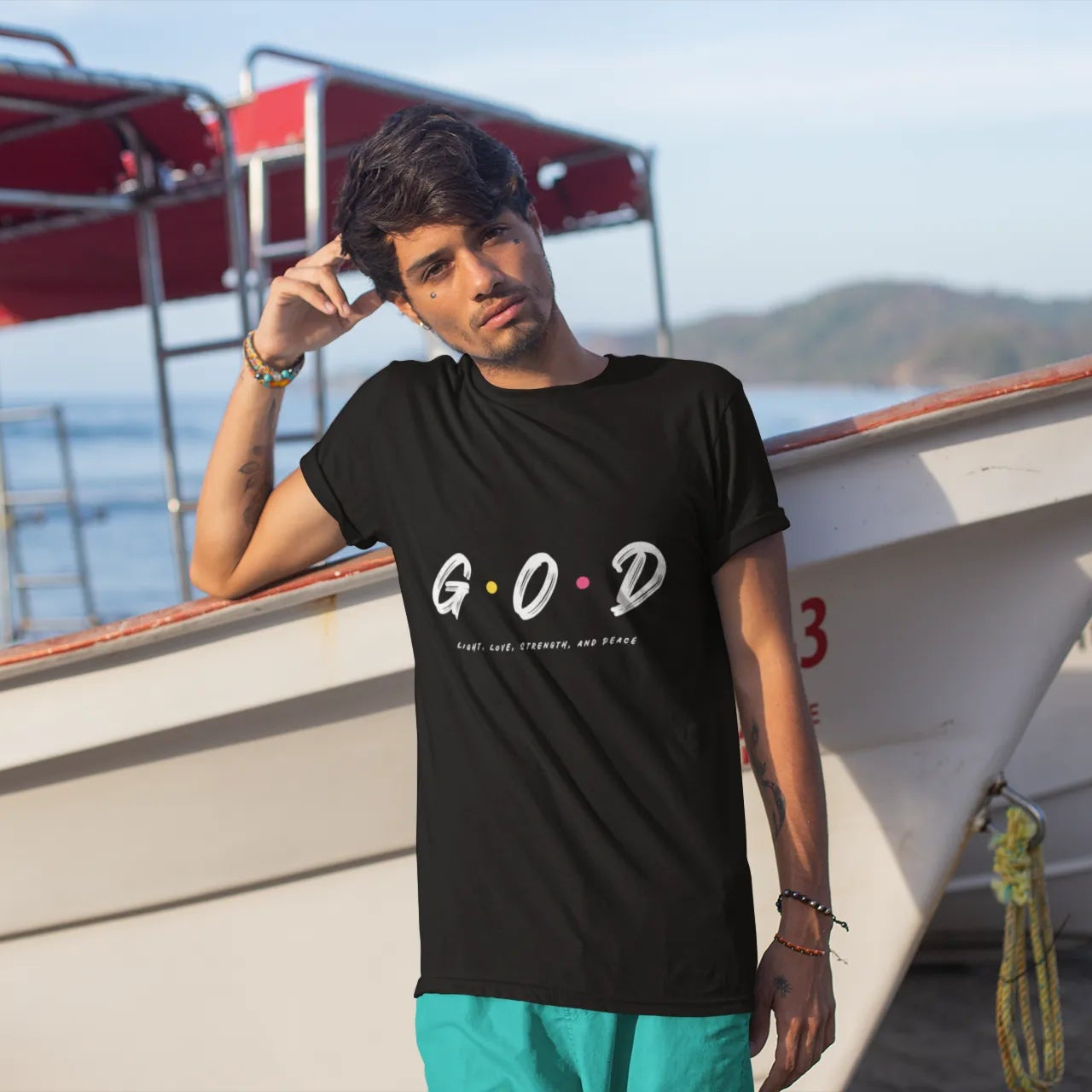 Person wearing a black t-shirt with 'G.O.D' text, standing near a boat on a beach.