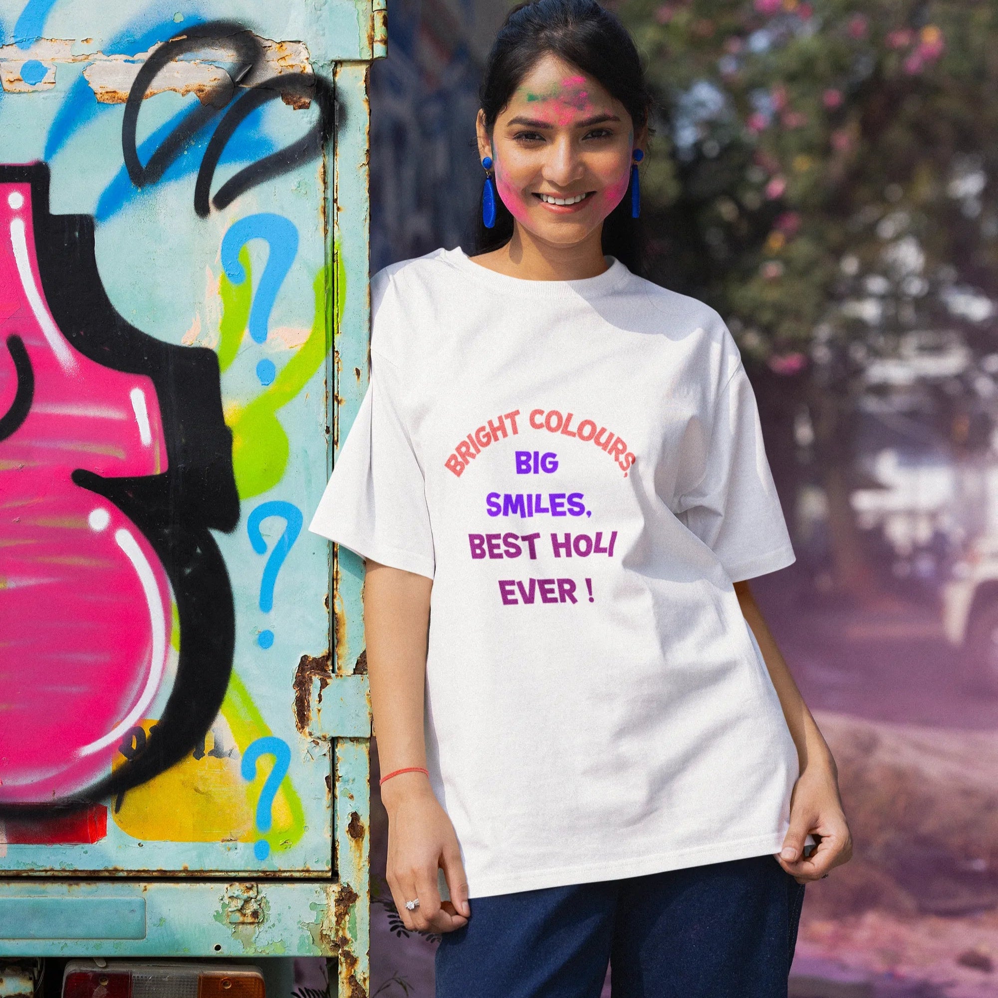 Woman wearing a white t-shirt with colorful text, standing in front of a graffiti-covered wall.