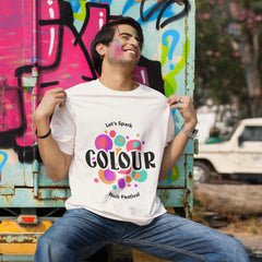 Person wearing a white t-shirt with colorful text, sitting in front of graffiti-covered metal sheets.