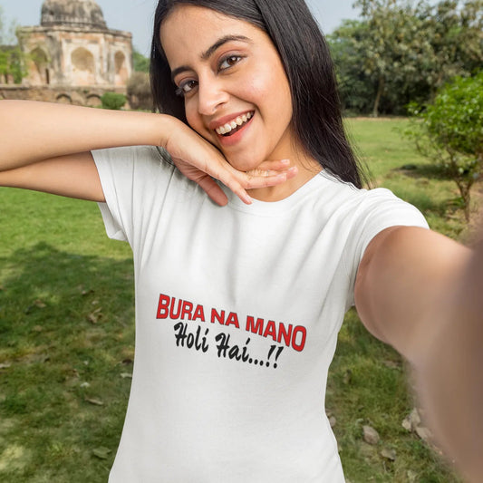 Woman wearing a white t-shirt with text, standing outdoors with greenery and a building in the background.