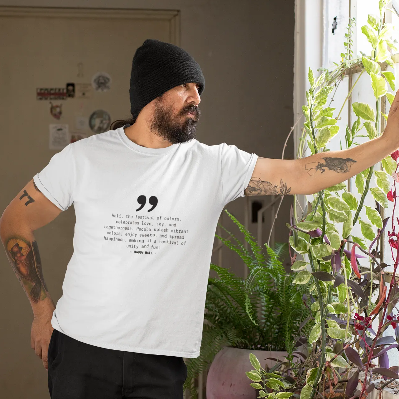 Man wearing a white t-shirt with text, standing indoors next to plants.