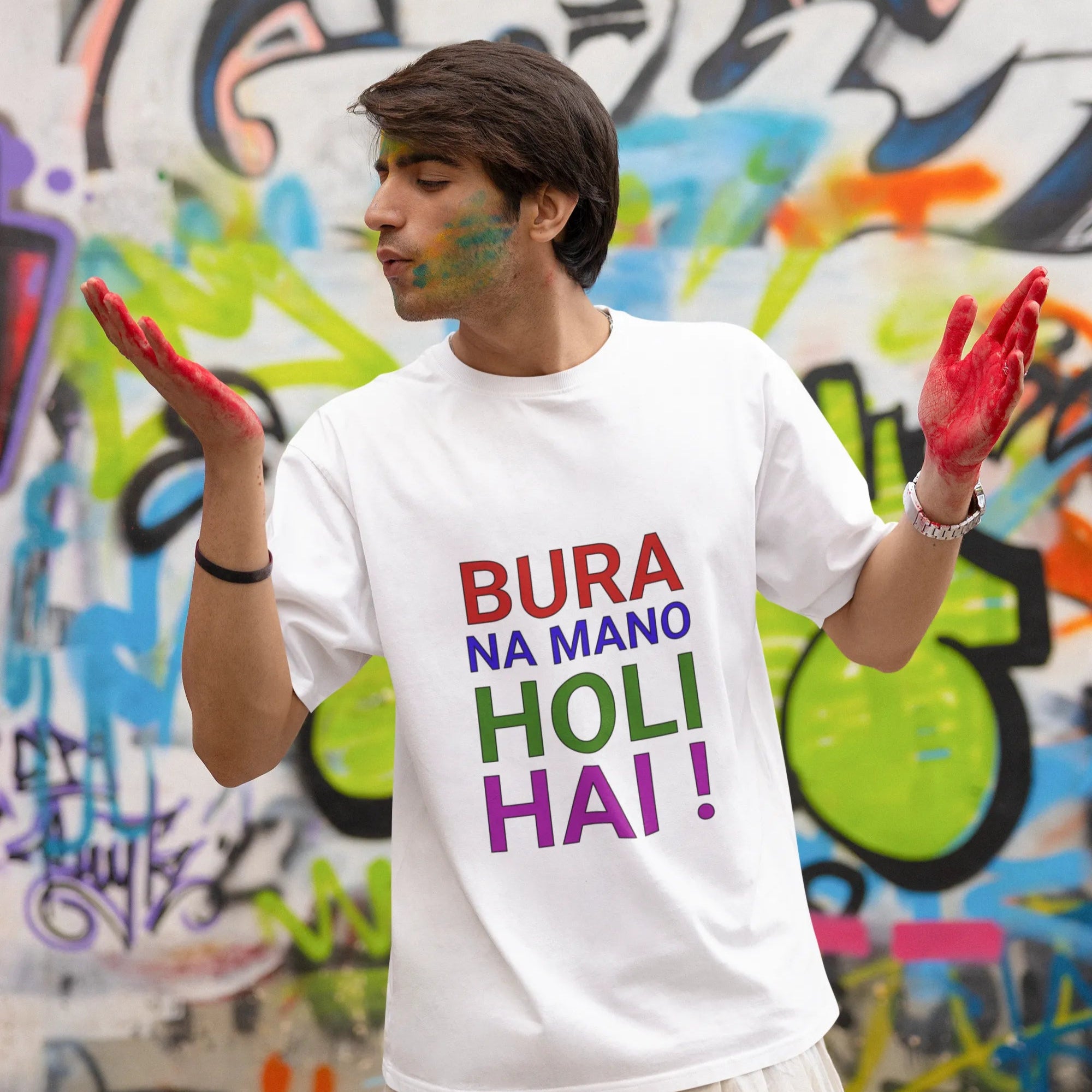 Person wearing a white t-shirt with colorful text in front of a graffiti wall