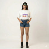 Person wearing a white t-shirt with 'Let's Play Holi!' text and denim shorts on a white background