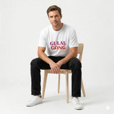 Man sitting on a chair wearing a white t-shirt with 'GULAL GANG' text.