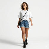 Woman wearing a white t-shirt, blue denim shorts, and black boots on a plain background