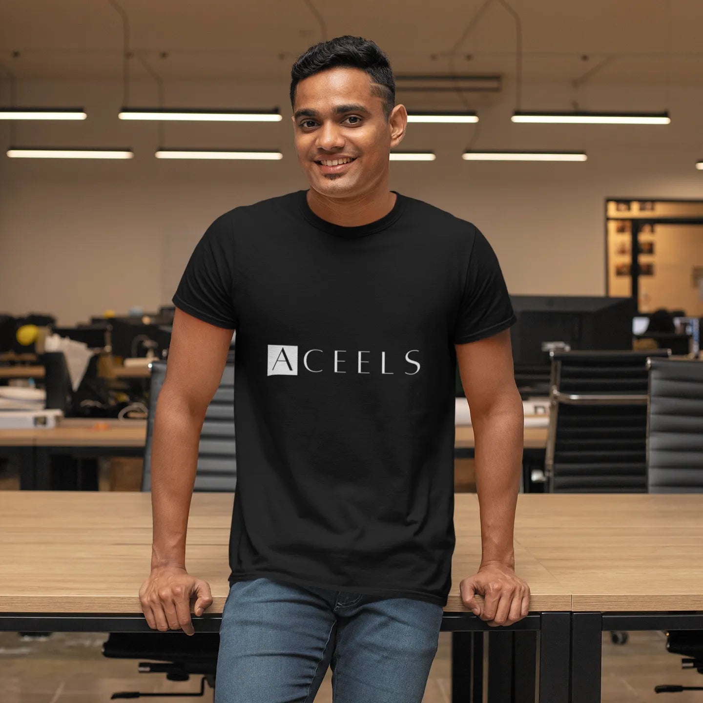 Man wearing a black t-shirt with 'ACEELS' logo in an office setting