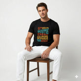 Man wearing a black t-shirt with colorful text design, sitting on a wooden stool against a white background.