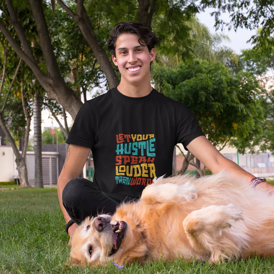 Person wearing a black t-shirt with colorful text, sitting on grass with a dog.